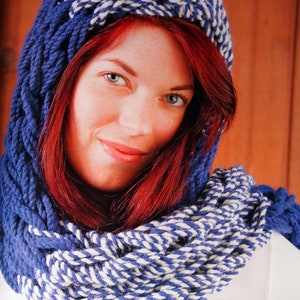 May include: A woman with long red hair is wearing a blue and white striped knitted scarf. The scarf is thick and chunky, and it is wrapped around her neck and shoulders.