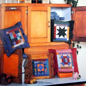 May include: A vintage wooden cabinet with two doors and shelves. The cabinet is decorated with four colorful patchwork pillows. The pillows are made of different fabrics and patterns. The cabinet is decorated with a sign that says "COUNTRY CHARM".