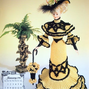 May include: A crocheted doll in a yellow and black Victorian-style dress, hat, and parasol. The doll is part of a calendar page for January 1996. A small fern and a decorative statue are in the background.