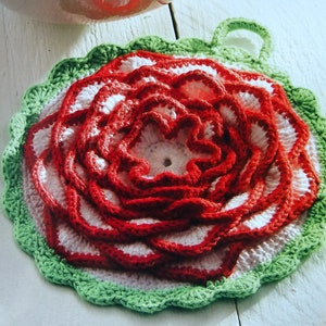 May include: A crocheted pot holder shaped like a flower with red, white and green layers. The pot holder has a loop handle.