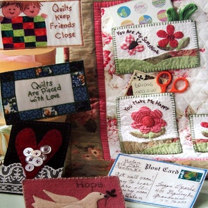 May include: A book cover titled "Quilted Post Cards" displaying handmade quilted postcards. The postcards feature designs with flowers, hearts, and messages such as "You Are My Sunshine" and "Hope".