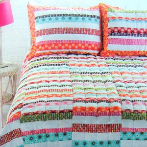May include: A white and multi-colored striped quilt with a white background. The quilt has a variety of colorful stripes, including pink, orange, green, and blue. The quilt is made of cotton fabric and has a quilted design. The quilt is shown on a bed with two matching pillowcases.
