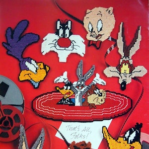 May include: A collection of Looney Tunes character needlepoint designs on a red background. Characters include Bugs Bunny, Daffy Duck, Sylvester, and others. The phrase "That's All, Folks!" is written on a small white card.