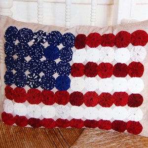 May include: A decorative pillow with a red, white, and blue American flag design. The flag is made of fabric circles sewn together.