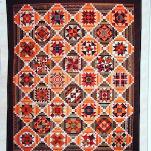 May include: A sampler quilt titled Golden Memories featuring a grid of square blocks with geometric star patterns in shades of orange, brown, red, and cream. The quilt has a dark brown border and measures 64.5 inches by 79.5 inches as printed.