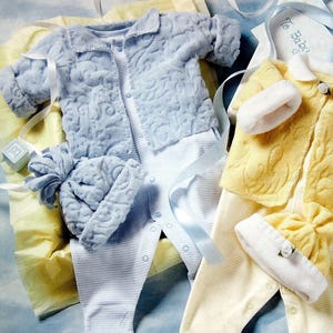 Peut inclure: Deux tenues de bébé, une bleue et une jaune, avec des bonnets assortis. Les tenues sont en tissu doux et texturé et présentent un joli motif brodé. Les tenues sont présentées sur un fond blanc avec des rubans bleus et blancs.