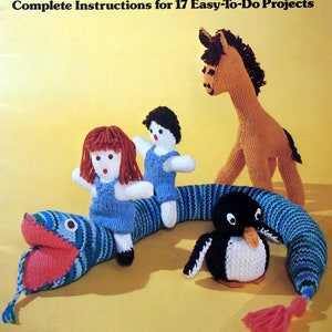 May include: A book cover with the title "Nellie Burnham Knitted Toys and Dolls" and a subtitle "Complete Instructions for 17 Easy-To-Do Projects". The cover features a colorful knitted snake, a penguin, a doll, and a horse.