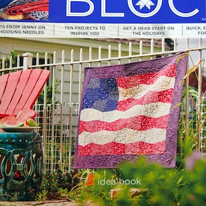 Op de afbeelding: Een tijdschriftcover met de titel "BLOCK" in een wit, gestikt lettertype. Het tijdschrift gaat over quilten en toont een rood-wit-blauwe patchworkdeken in de vorm van een Amerikaanse vlag die aan een wit hek hangt. De tijdschriftcover bevat ook de tekst "Missouri Star Quilt Co."