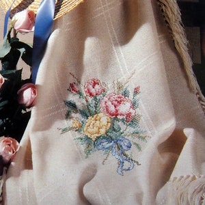 May include: A white crocheted throw blanket with a fringe border and a floral embroidery design. The embroidery features a bouquet of pink, yellow, and red flowers with a blue ribbon.
