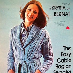 Op de afbeelding: Een lichtblauwe kabelgebreide sweaterjas met een sjaalkraag, zakken en een strikceintuur. De jas maakt deel uit van een breipatroonboekje. De tekst op de afbeelding luidt "The Easy Cable Raglan Sweater Jacket."