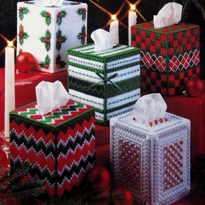 May include: An image of five festive tissue box covers in various designs. The covers are made of plastic canvas and feature holiday patterns in red, green, and white. The text "FESTIVE BOUTIQUES IN PLASTIC CANVAS" is at the top.