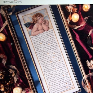 May include: A framed cross-stitch depicting an angel with a cherubic face and wings, set against a blue background within a gold frame. The artwork includes text, with the words "SPEAKING OF ANGELS" and "PRAYING HANDS" at the top of the frame.