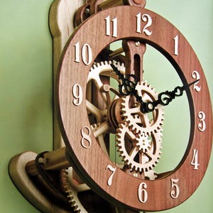 May include: A wall-mounted clock featuring a dark brown wooden circular frame with light-colored wooden numerals from 1 to 12. The clock displays an exposed internal mechanism with light-colored wooden gears and black ornate metal clock hands.