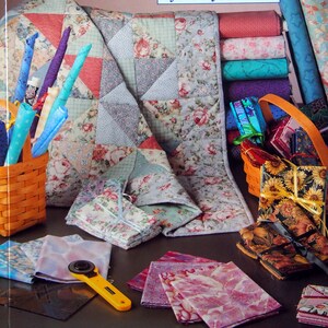 Puede incluir: Una portada de libro titulada "Fun with Fat Quarters" de Nancy J. Martin. La imagen presenta un edredón, rollos de tela y cestas llenas de paquetes de tela. Se muestran varias telas, incluyendo diseños florales y estampados, con un cortador rotatorio amarillo.