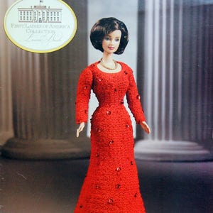 May include: A doll from the First Ladies of America Collection, Laura Bush edition, wearing a red textured gown with sparkling embellishments. The doll has short, dark hair and a gold necklace. The packaging includes the White House seal.