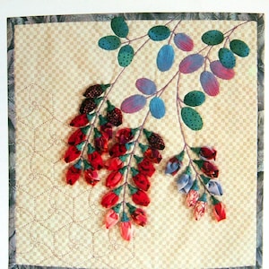 Op de afbeelding: Een gequilte wandhanger met een bloemenmotief. De bloemen zijn gemaakt van stof en zijn in tinten rood, roze, blauw en groen. De achtergrond is een beige en bruin geruit patroon.