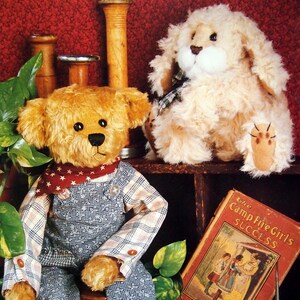 Könnte beinhalten: Zwei Plüschtiere: ein Teddybär mit Latzhose und ein Hund. Der Teddybär hat einen roten Schal mit Sternenmuster und sitzt mit einem Buch mit dem Titel "The Camp Fire Girls Success". Der Hund ist flauschig und hellbraun.