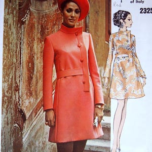 May include: A vintage Vogue Couturier Design fashion illustration. The image features a woman in a coral-colored coat and matching hat. The coat has a high collar and button details. A smaller illustration shows a patterned dress. Text includes "Fabiani of Italy" and "2325."