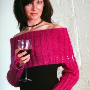 May include: A vibrant magenta off-the-shoulder knitted shrug featuring a ribbed texture and long sleeves with thumb holes. The garment is embellished with small, clear, reflective sequins arranged in vertical rows along the cuffs and lower edge.