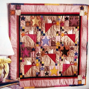Peut inclure: Une courtepointe en patchwork avec une bordure rose et un motif central d'étoiles et d'anges. La courtepointe est intitulée "Amalie's Angels".