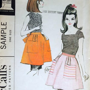 May include: Vintage McCall's printed pattern for Misses' and Junior short aprons. The illustration shows two aprons, one orange and one pink, with a black and white top. The pattern is marked "Sample" and "One Size."