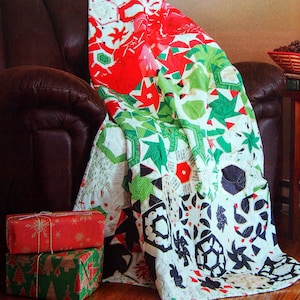 May include: A colorful Christmas-themed quilt draped over a brown leather armchair. The quilt features red, green, and white geometric patterns with stars and other festive shapes. Two wrapped gifts with holiday paper are in the foreground.