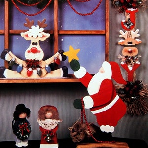 May include: Wooden Christmas decorations featuring a reindeer, Santa Claus, and two dolls. The reindeer holds a string of lights, and Santa holds a star and a string of red beads. A garland of lights and red beads hangs above the reindeer.