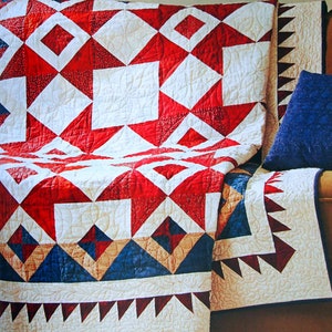 May include: A red, white, and blue patchwork quilt with a geometric pattern. The quilt is folded over a couch with a blue pillow.