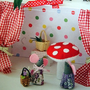May include: Two felt mice wearing dresses and carrying baskets stand in front of a red and white mushroom. The scene is set in a miniature dollhouse with red and white gingham curtains and a polka dot wallpaper.