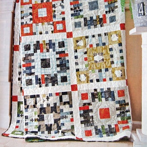 May include: A patchwork quilt with a white background and squares of various colours and patterns, including red, black, white, blue, and green. The quilt is made up of smaller squares that are sewn together to create a larger design.