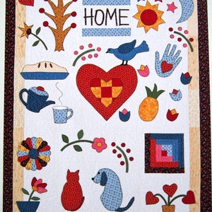 Op de afbeelding: Een kleurrijk patchwork-deken met verschillende ontwerpen, waaronder een hart, een boom, een vogel, een ananas, een taart, een theepot, een kopje, een bloem, een kat, een hond en het woord "HOME".