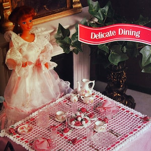 May include: A white crocheted tablecloth with a pink and red floral design. The tablecloth is set with a tea set, including a teapot, cups, and saucers. The text "Delicate Dining" is displayed on a red banner.