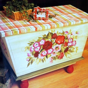 May include: A hand-painted wooden storage chest with a plaid top and floral design. The chest has red, green, and white accents and sits on four red wooden legs.