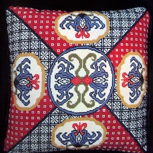 May include: A square pillow with a red, white, and blue geometric pattern. The pattern features stylized floral motifs and a central circle with a cross-shaped design.