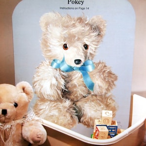 Peut inclure: Un ours en peluche blanc nommé "Pokey" avec un ruban bleu autour du cou. L'ours est assis sur une surface blanche avec un fond bleu. Le texte "Instructions on Page 14" est imprimé sur la surface.