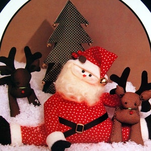 May include: A red and white Santa Claus doll with a white beard and a black hat sits in the snow with two reindeer dolls. The Santa doll is holding a bell in one hand. The reindeer dolls are brown and black with red noses.