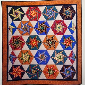 May include: A quilt titled "Pin Reel" featuring a geometric pattern of colourful hexagons with a star design. The quilt is made with a variety of fabrics in shades of red, orange, yellow, green, blue, and black.
