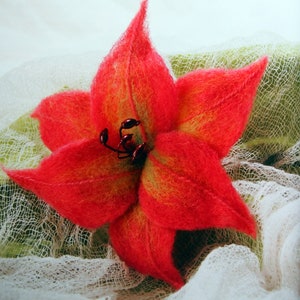 Op de afbeelding: Een handgevoelde rode en gele lelie met een parelmoer hart. De bloem ligt op een witte stoffen achtergrond.