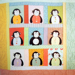 May include: A patchwork quilt with a colorful design featuring nine monkeys wearing different colored shirts. The quilt is made of various fabrics with different patterns and textures.