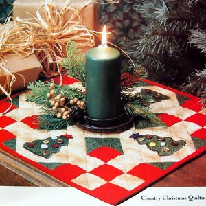 Può includere: Un runner da tavolo trapuntato rosso, bianco e verde con un design a forma di albero di Natale. Il runner è decorato con bottoni e una candela verde è al centro.