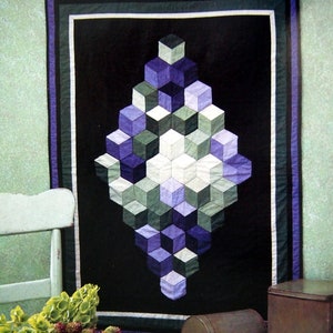 May include: A quilt with a geometric design of cubes in shades of purple, green, and white. The quilt is framed with a black border and a green and white border.