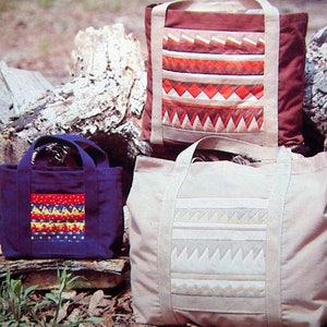May include: Three tote bags with different geometric patterns. The bags are made of canvas and have brown, beige, and blue fabric. The bags are sitting on a pile of logs.