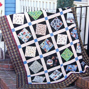May include: A black and white quilt with a plaid border. The quilt is made up of squares with different patterns, including animals, trees, and houses. The quilt is displayed on a porch.