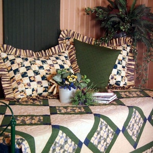 May include: A cream-coloured quilted bedspread with green and blue diamond patterns. Two pillows with floral patterns and a green pillow are on the bed. A potted plant and three books are on the bedspread.