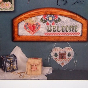 May include: A collection of cross-stitch patterns featuring hearts, houses, and the word "WELCOME". The patterns are framed and displayed on a blue background. The title "HeartStrings" and "A Paper Potpourri" are printed at the top of the page. The text "The Artists Collection... presents Pat Thode" is printed at the bottom of the page.