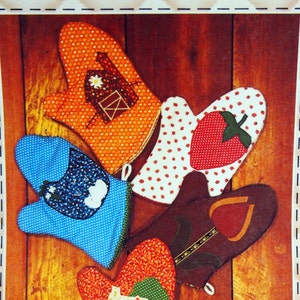 May include: A vintage craft pattern for making four different hot pads. The pattern features a red and white polka dot hot pad with a strawberry applique, a blue hot pad with a cloud applique, a brown hot pad with a pear applique, and an orange hot pad with a house applique. The pattern is titled "Mitt Hot Pad" and is from "Patch Press".