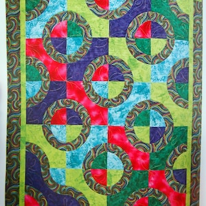 May include: A rectangular quilt featuring a repeating pattern of circles and swirls in vibrant shades of red, green, blue, and purple. The design includes a border with a swirling motif and a grid of squares containing circular shapes.