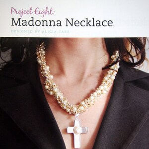 May include: A white pearl and gold bead necklace with a silver cross pendant. The cross has a large white pearl in the center.