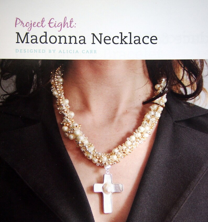 May include: A white pearl and gold bead necklace with a silver cross pendant. The cross has a large white pearl in the center.