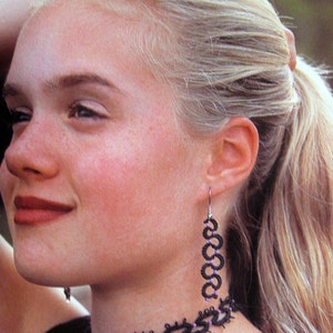 May include: A woman wearing a black choker necklace and matching dangle earrings. The necklace and earrings are made of black thread with purple accents.
